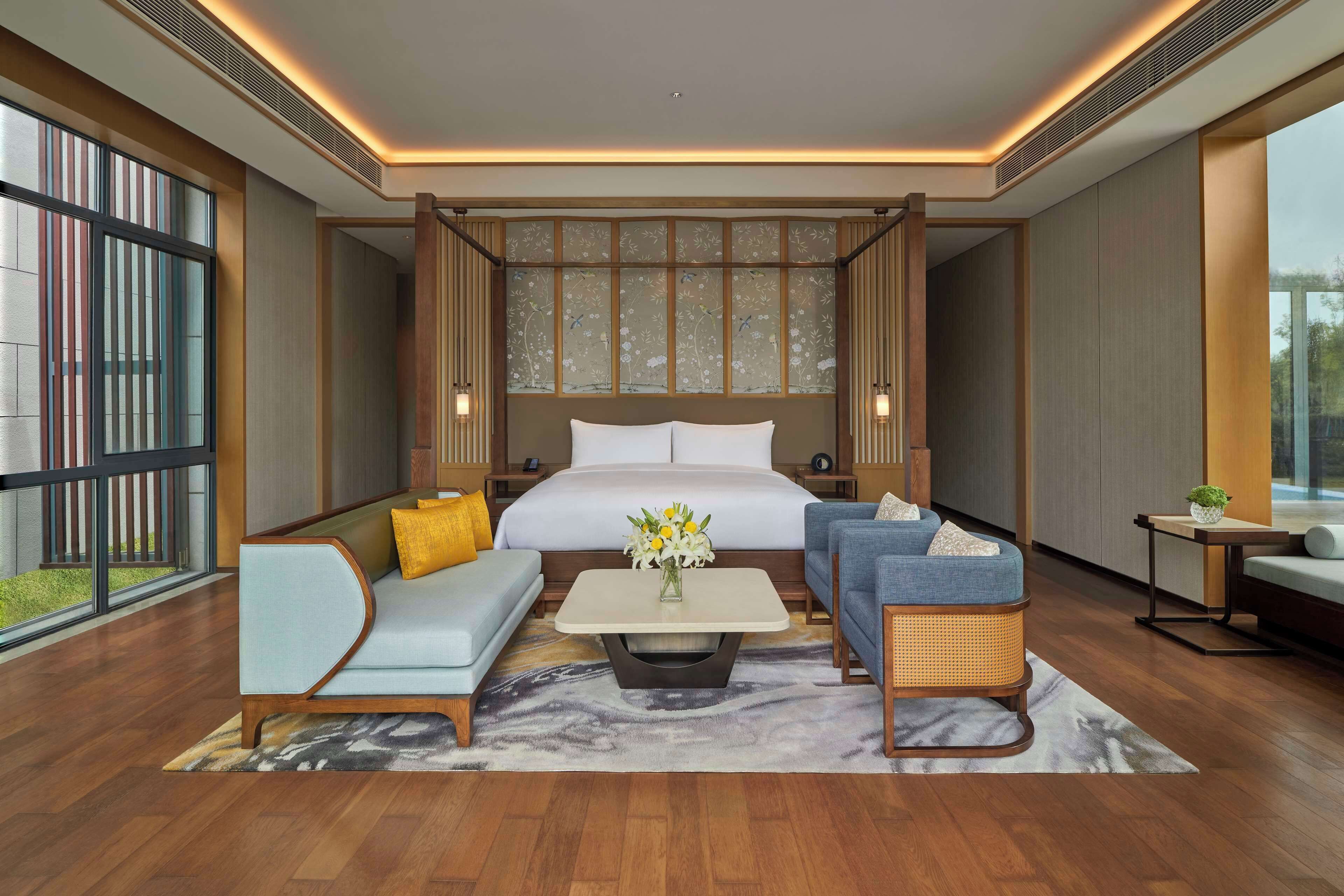 A modern hotel room with a large bed, two sofas, a coffee table, and a small side table.
