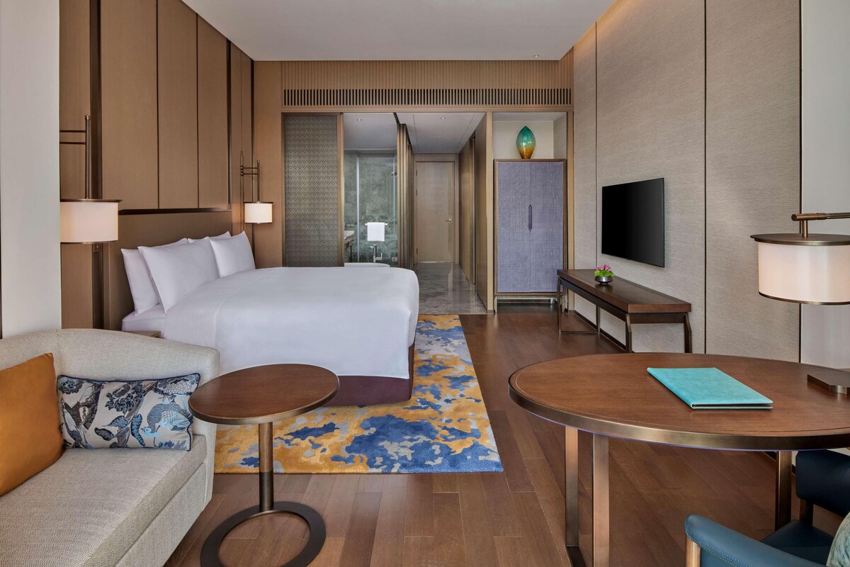 A hotel room with a large bed, a sofa, a dining table, and a TV.