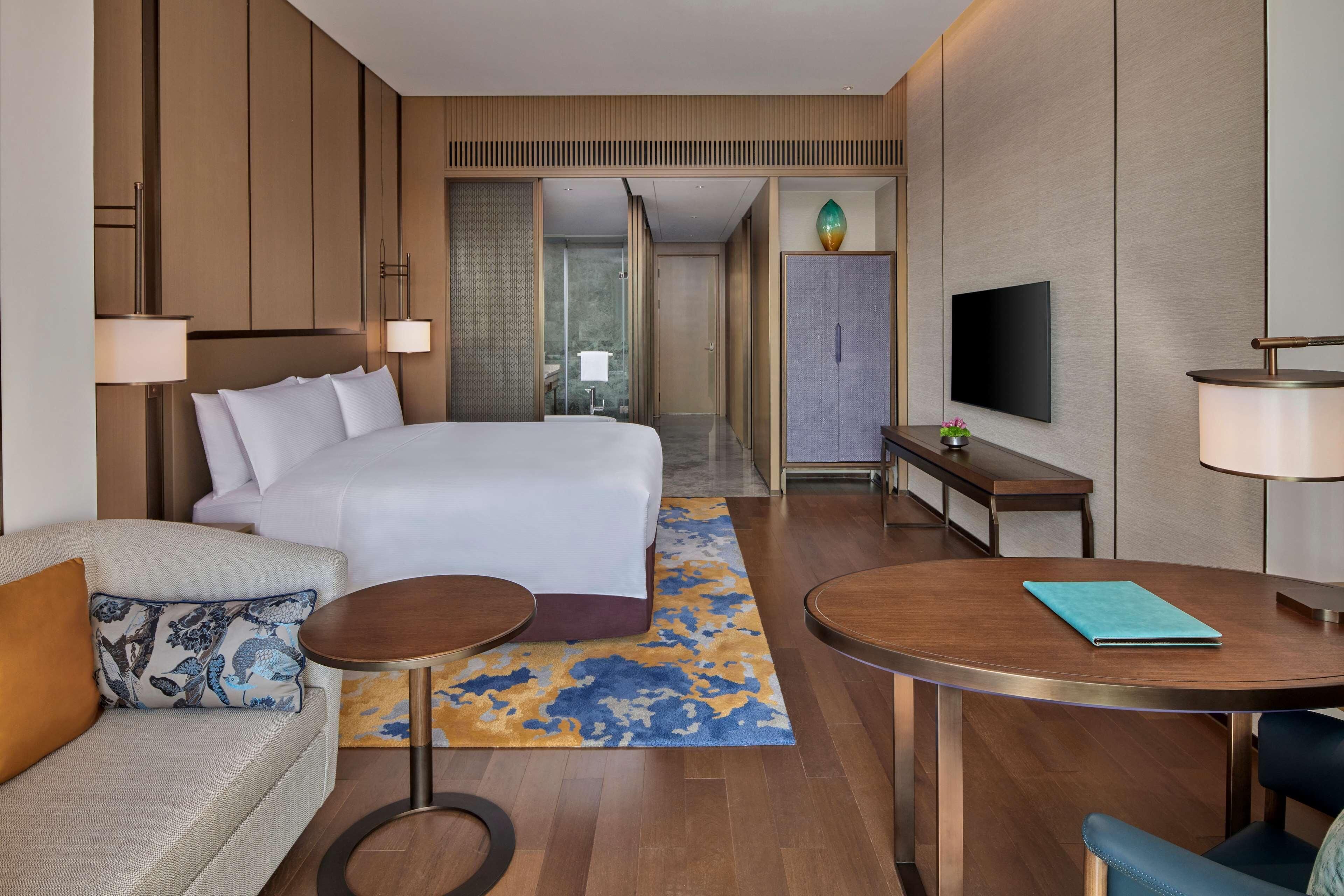 A hotel room with a large bed, a sofa, a dining table, and a TV.