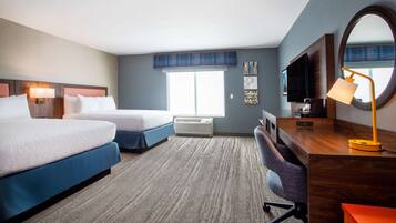 A hotel room with two beds, a desk with a chair, a TV, a lamp, and a large window.