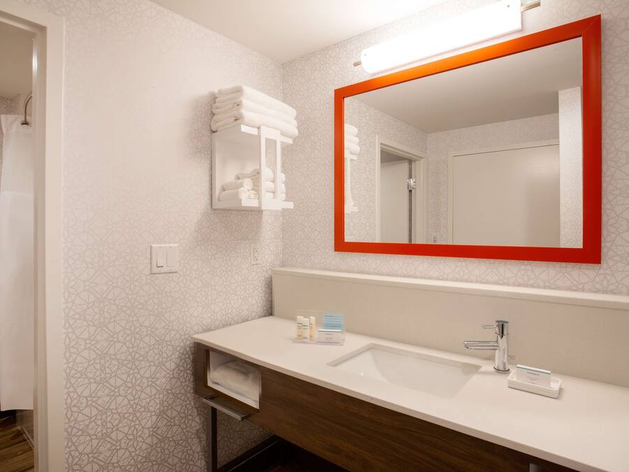 Une salle de bain moderne avec un lavabo blanc, un miroir à cadre rouge et un porte-serviettes.