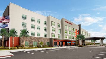 Hampton Inn features a flat roof and windows on each floor, surrounded by a parking lot and lush landscaping.