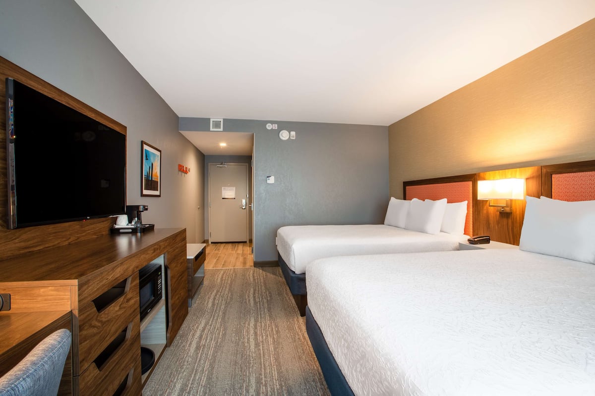 Ein Hotelzimmer mit Fernseher, Schreibtisch mit Kaffeemaschine, zwei Betten und einem Holzkopfteil.