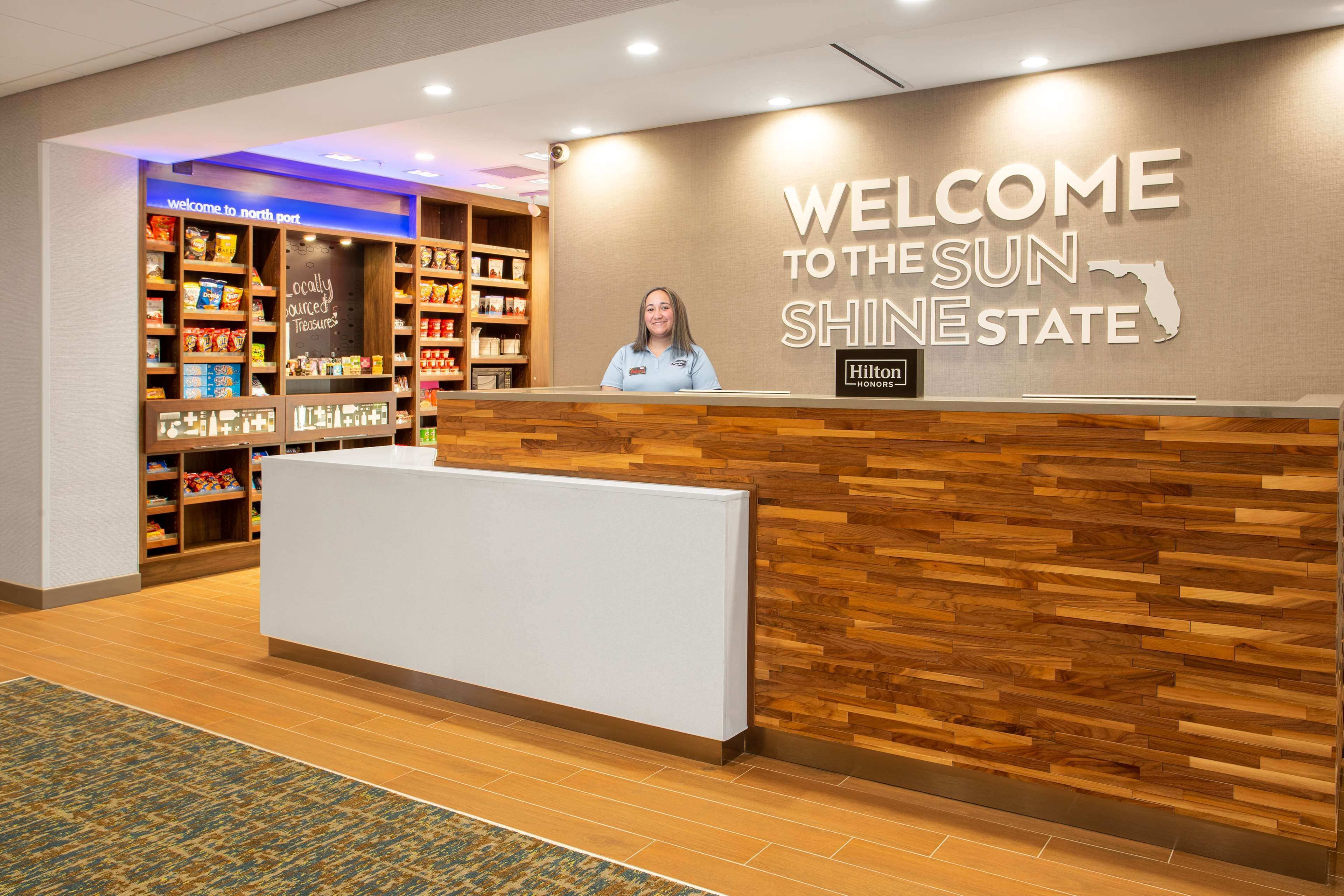 Un mostrador de recepción con diseño de panel de madera, un letrero que dice "WELCOME TO THE SUN SHINE STATE" y el logotipo de Hilton Honors.