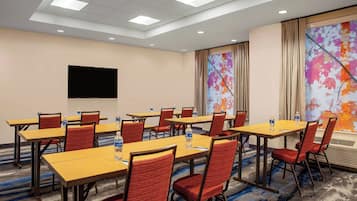 A conference room with multiple tables and chairs, a flat-screen TV, and a large floral painting on the wall.
