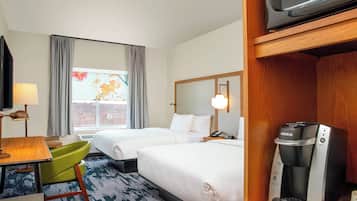 A hotel room with two beds, a desk, a chair, a coffee maker, and a television.
