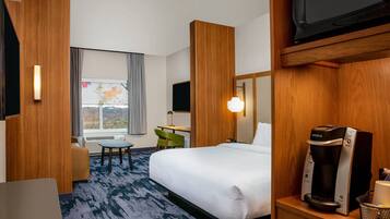 Habitación de hotel con cama, escritorio, silla, cafetera y televisor.