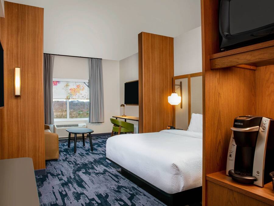 A hotel room with a bed, a desk, a chair, a coffee maker, and a television.