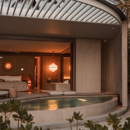 A modern, curved building with a pool, a bedroom with a large bed, and a bathroom with a vanity.