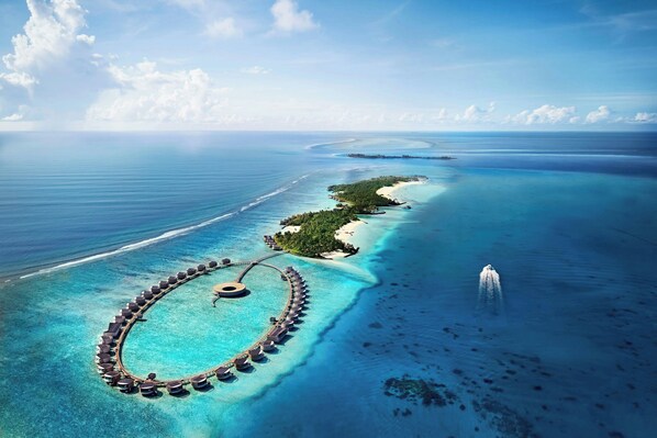 An aerial view of a resort island with a circular waterway, overwater bungalows, and a central circular structure.