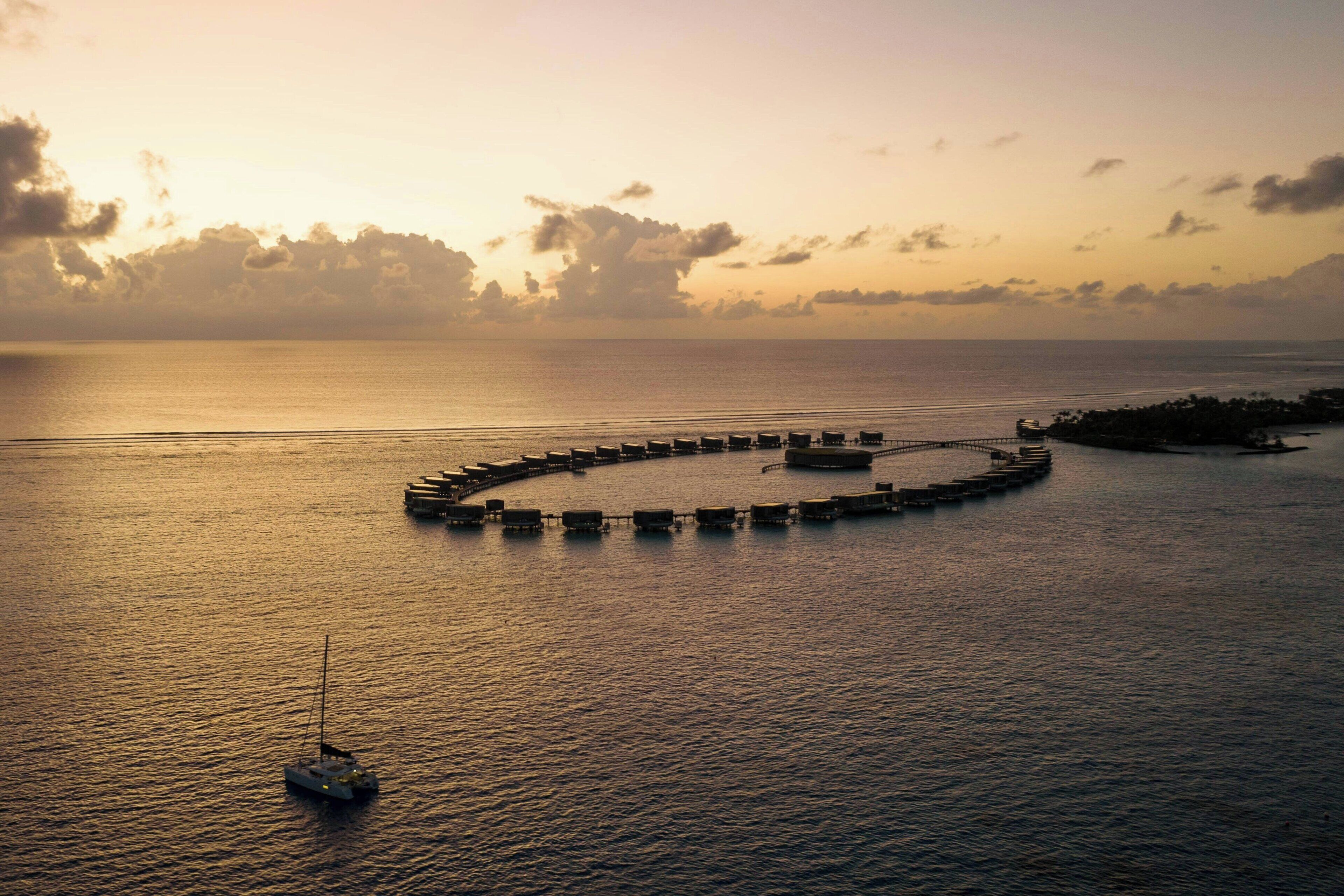 Vista aérea de una estructura portuaria circular rodeada de agua tranquila, con un barco en primer plano.