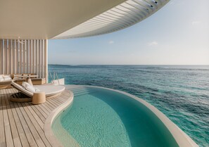 A luxurious outdoor deck with a curved infinity pool, lounge chairs, and a view of the ocean.