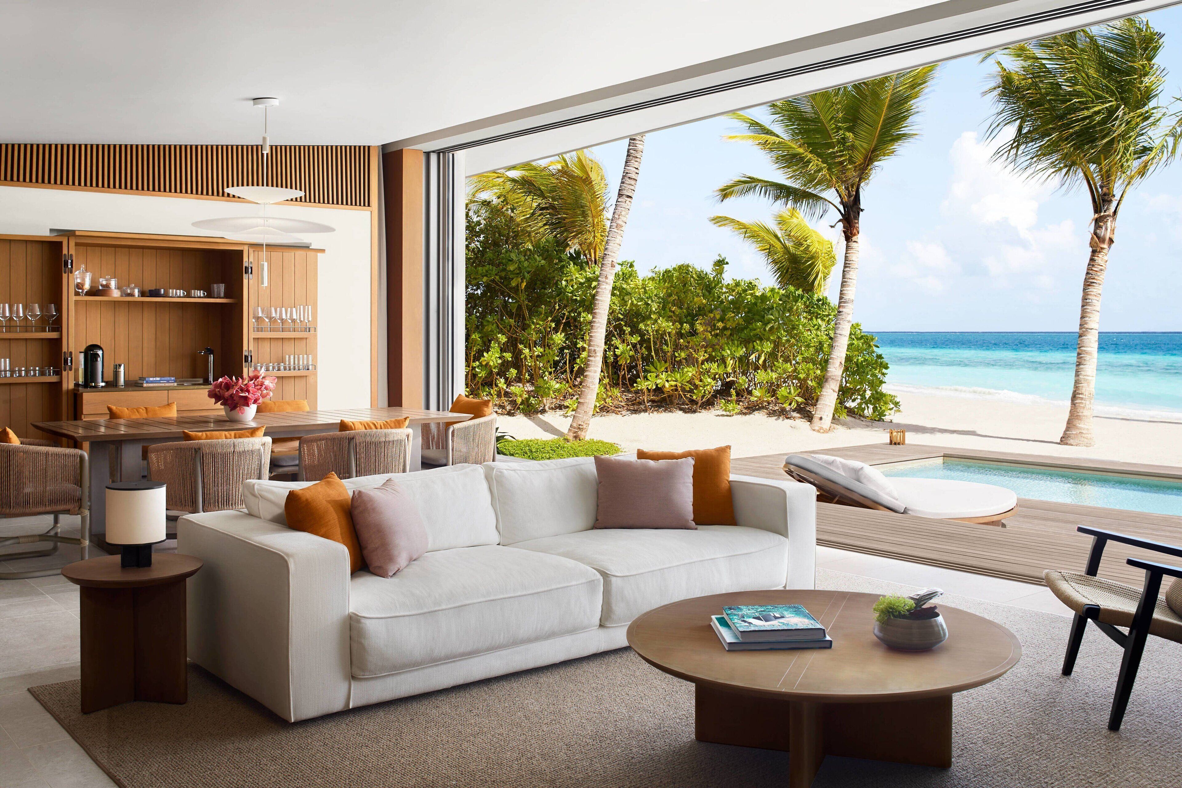 Ein modernes Wohnzimmer mit großem Fenster, das Blick auf Strand und Pool bietet.