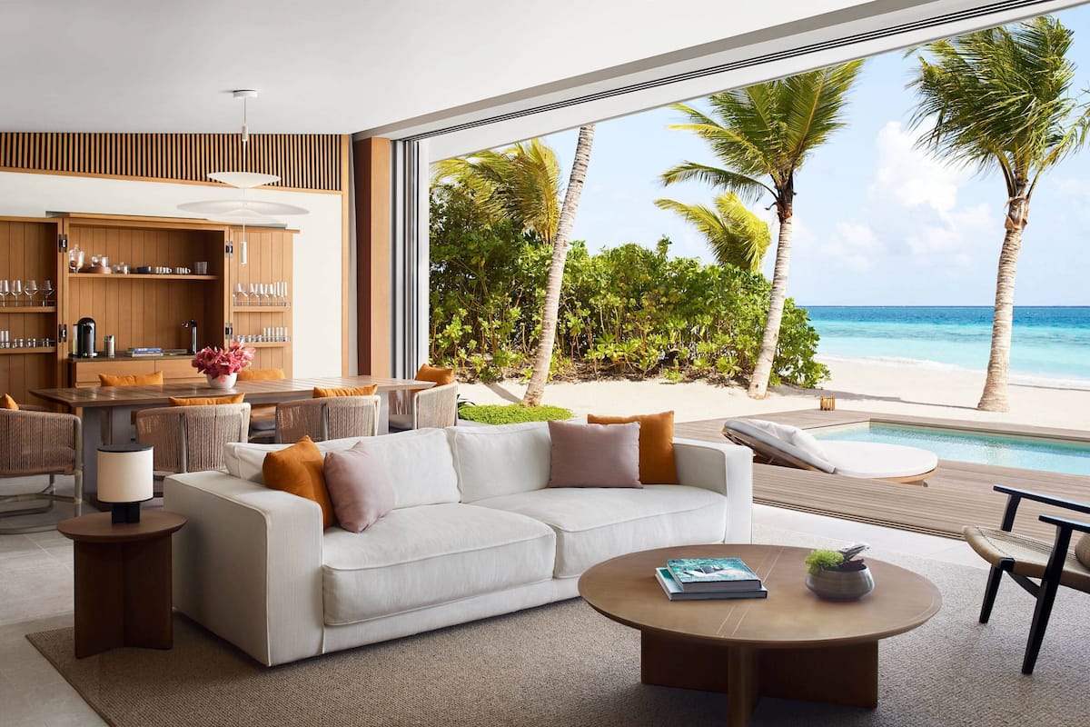 Un salon moderne doté d’une grande fenêtre donnant sur une plage et une piscine.