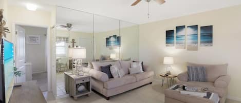 A living room with a beige sofa, a coffee table, a TV, and a ceiling fan.