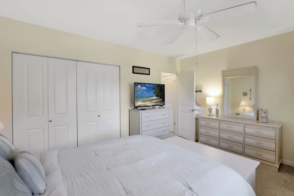 A bedroom with a bed, a TV, a dresser, a mirror, and a ceiling fan.
