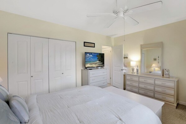 A bedroom with a bed, a TV, a dresser, a mirror, and a ceiling fan.