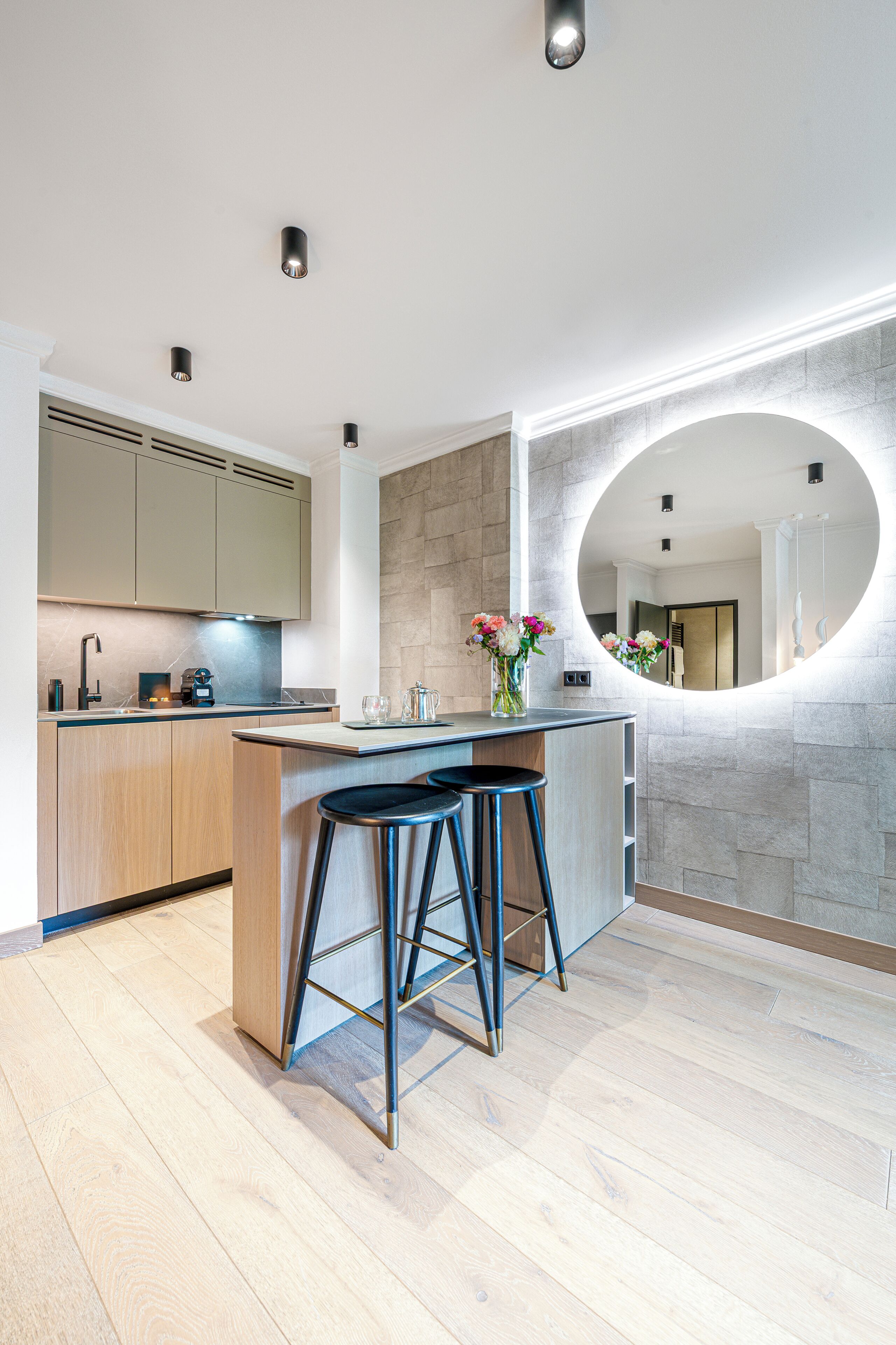 Une cuisine moderne avec un îlot central, des tabourets de bar, un miroir rond et un vase rempli de fleurs.
