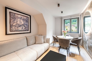 Una sala de estar moderna con un sofá, una mesa de comedor con sillas, una obra de arte enmarcada y un ventanal con vistas a edificios.