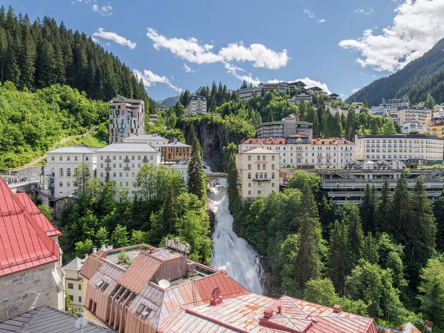 Uma cidade com edifícios, uma cascata e colinas arborizadas.