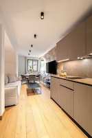 A modern kitchen with a dining area, wooden flooring, and a flat-screen TV.