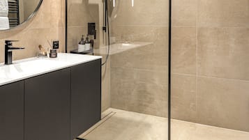 Un baño moderno con ducha envuelta en vidrio, un espejo redondo y un tocador de tonos oscuros.