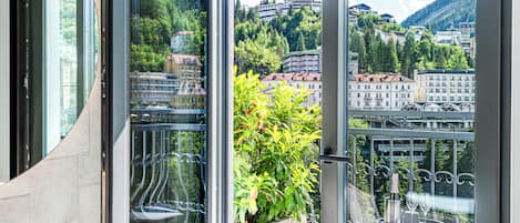A modern balcony with a glass door, a marble table, and a view of a cityscape with buildings and greenery.