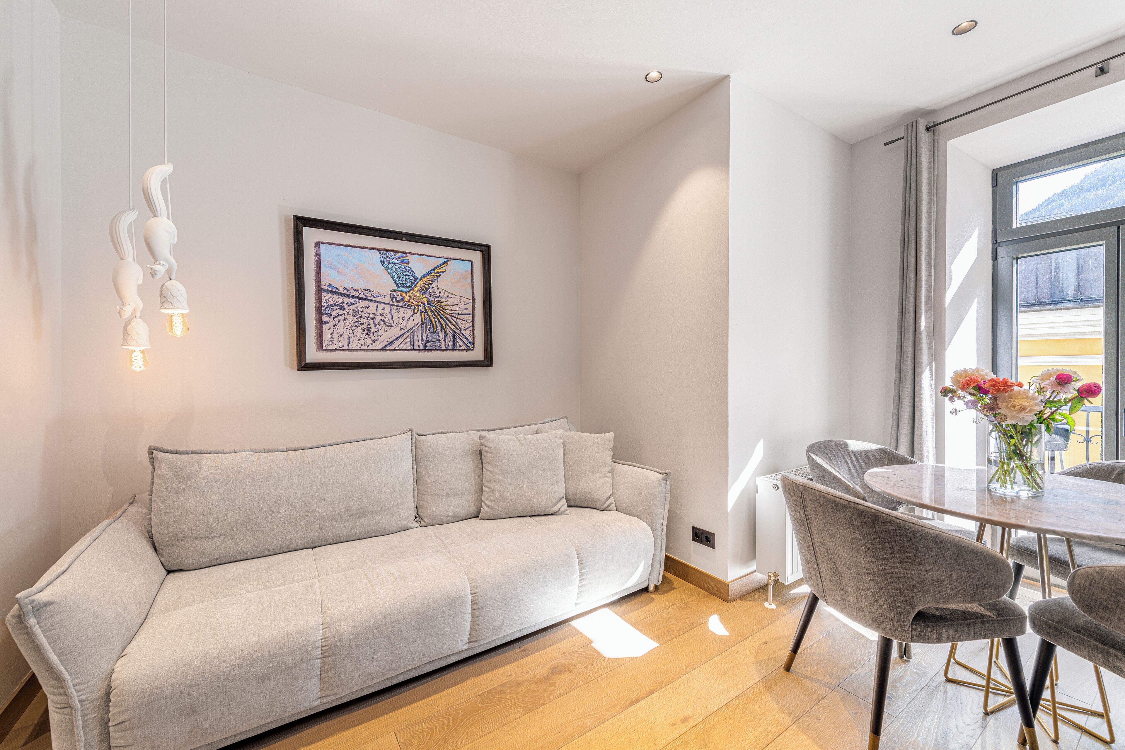 A modern living room with a sofa, dining table, chairs, and a framed artwork on the wall.