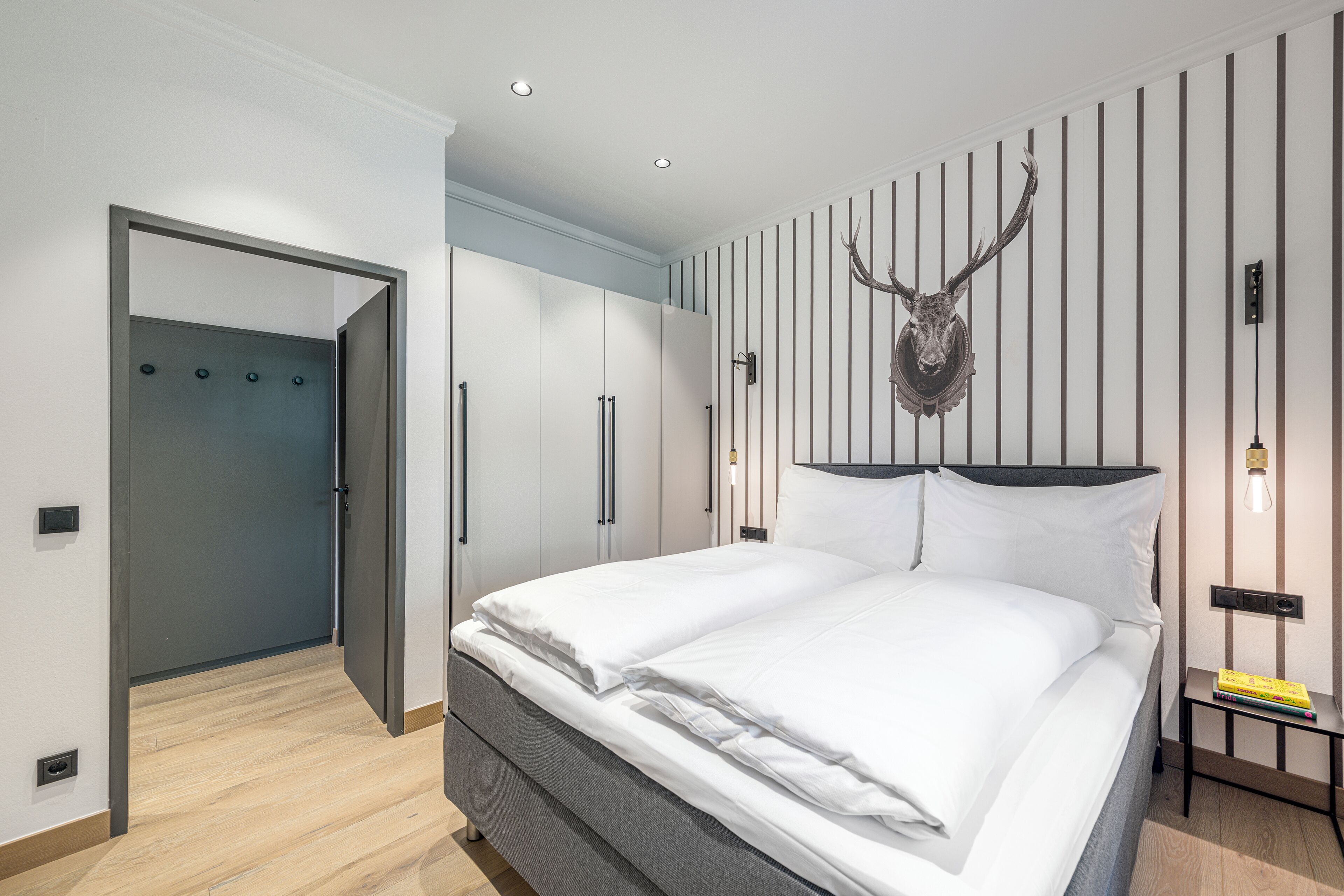 A modern bedroom with a large bed, a wardrobe, and a unique wall-mounted deer head decoration.