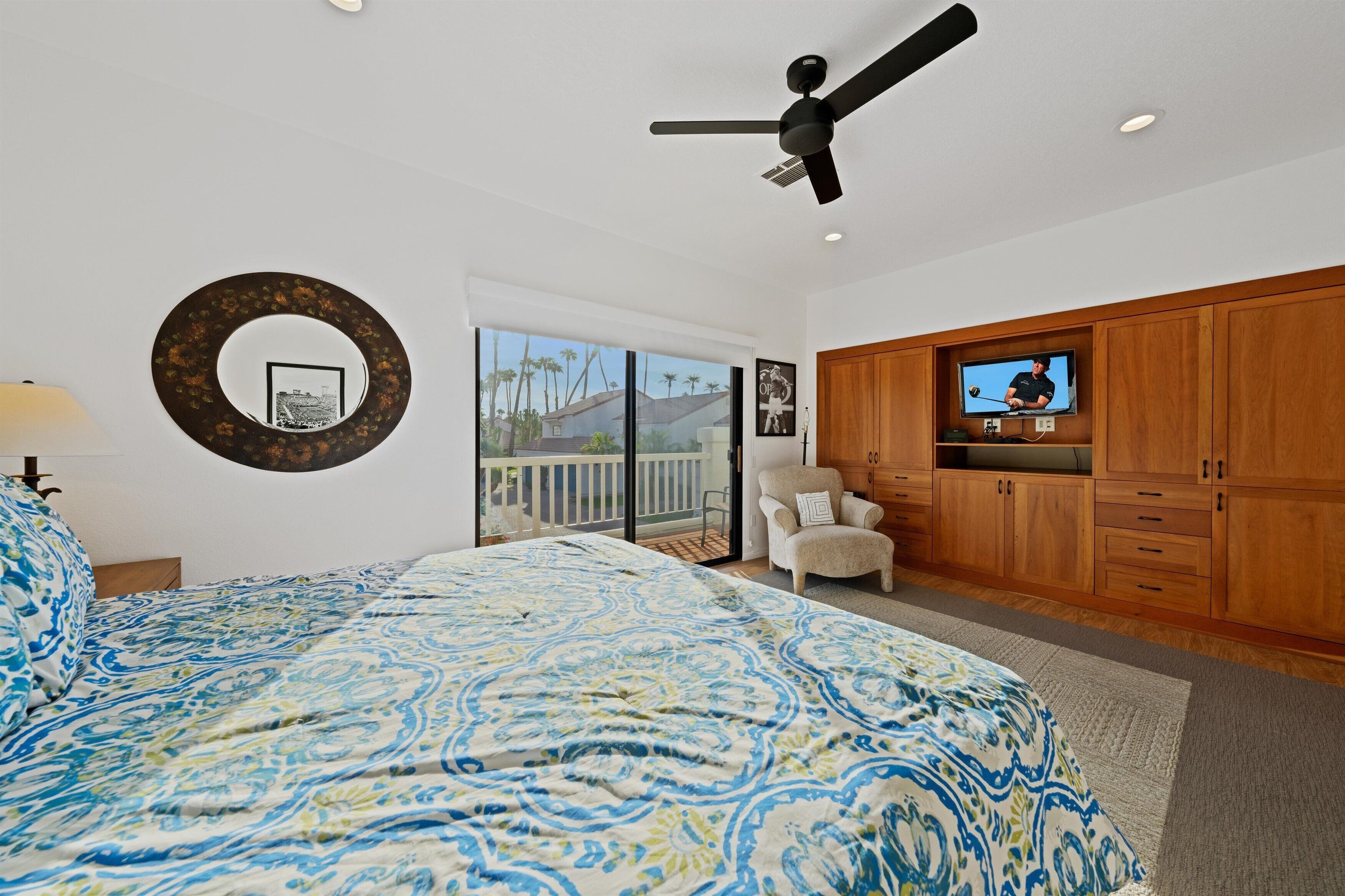 Un dormitorio con una cama grande, un ventilador de techo, televisión, armarios de madera y vistas al exterior.