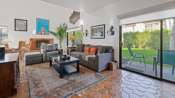 A spacious living room with a fireplace, comfortable seating, and a large sliding glass door leading to a patio. - Tennis Villa #18, 2 Bedrooms,  2.5 Baths Tennis Villa, Permit 063439 (La Quinta)