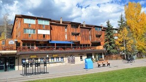 Un bâtiment en bois à plusieurs étages, doté d’un espace extérieur couvert avec des sièges et d’un auvent bleu.