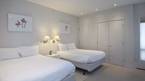 Une chambre d’hôtel avec deux lits, une table de chevet avec des lampes, une armoire et des œuvres d’art accrochées aux murs.
