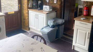 A kitchen with white cabinets, a table with a floral tablecloth, a washing machine, and a fire extinguisher.