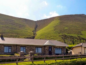 A stone building with a flat roof, a fenced yard, and a valley with hills in the background. - The Lodge Rossbeigh (Glenbeigh)