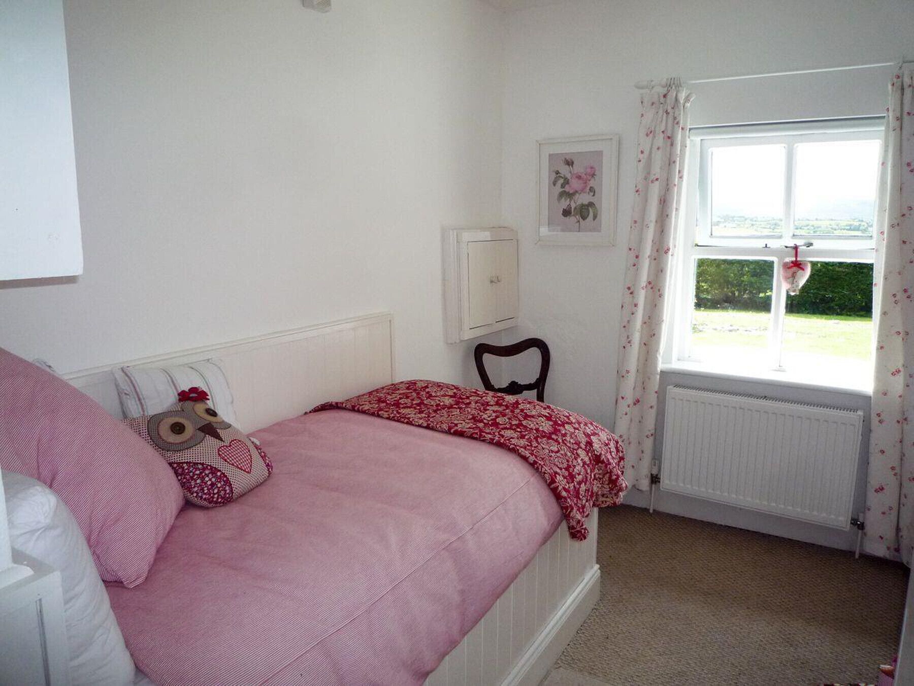 Un dormitorio con una cama individual, un radiador, una ventana con cortinas y un cuadro en la pared.