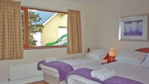Una camera d'albergo con due letti, una finestra con tende, un termosifone, una lampada e un quadro appeso al muro.
