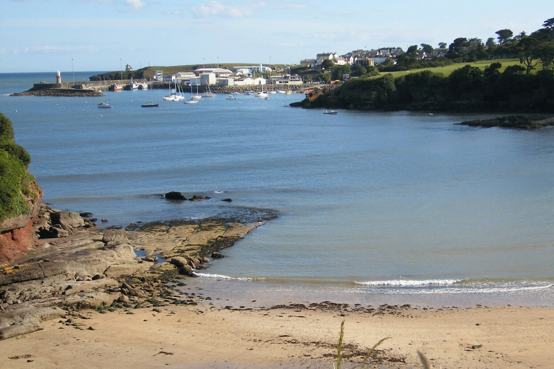 A coastal scene with a lighthouse, boats, and a town in the background.