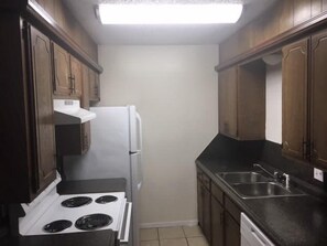 A compact kitchen with a white stove, a refrigerator, and a sink.