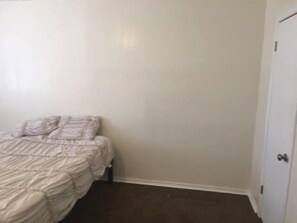 A bedroom with a bed, a door, and a plain wall.