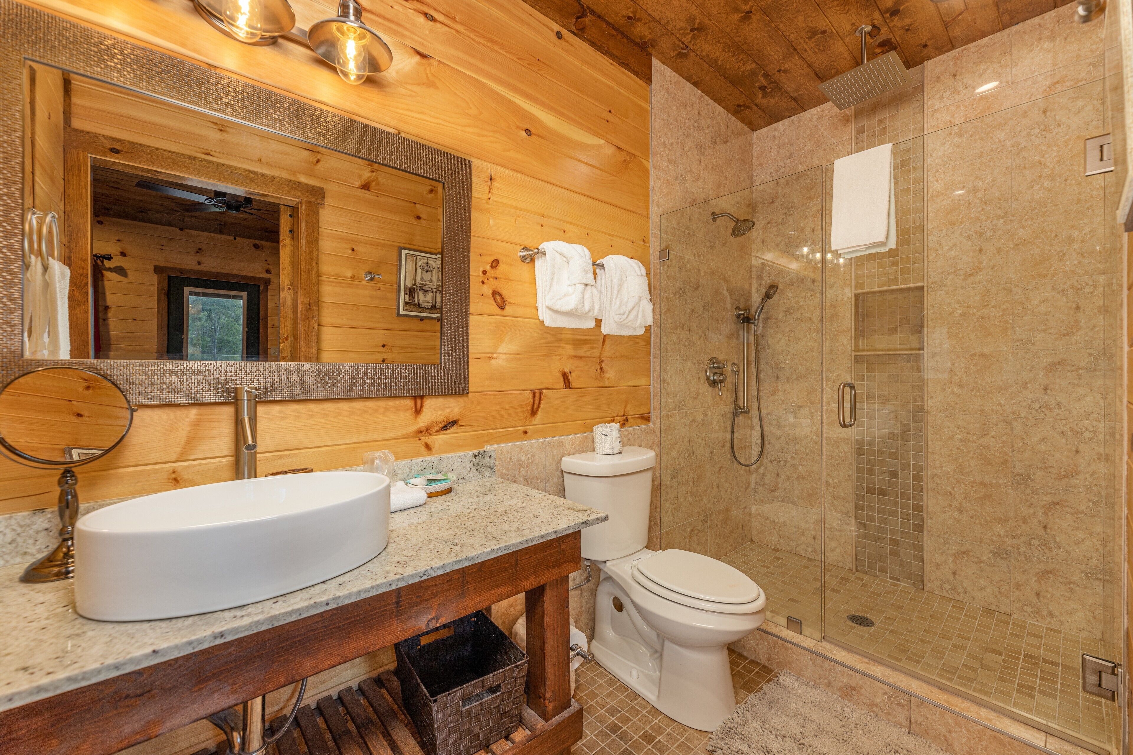 Baño de cabaña de madera con lavamanos grande, inodoro y ducha a ras de suelo.