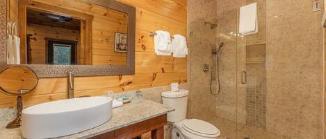 Baño de cabaña de madera con lavamanos grande, inodoro y ducha a ras de suelo.