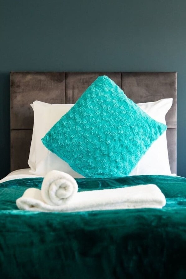 A bed with a teal throw pillow, a rolled white towel, and a teal bedspread. - Immaculate 5-bed House in the City Centre Ashford (Ashford)