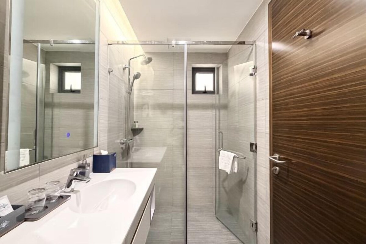 A modern bathroom with a glass shower enclosure, a large mirror, and a wooden panel wall.