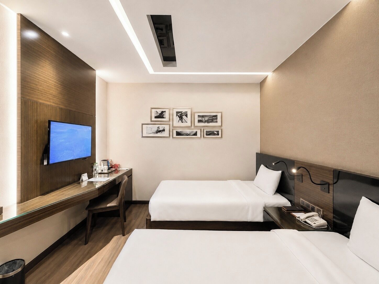 A hotel room with a desk, two beds, a TV, and framed pictures on the wall.