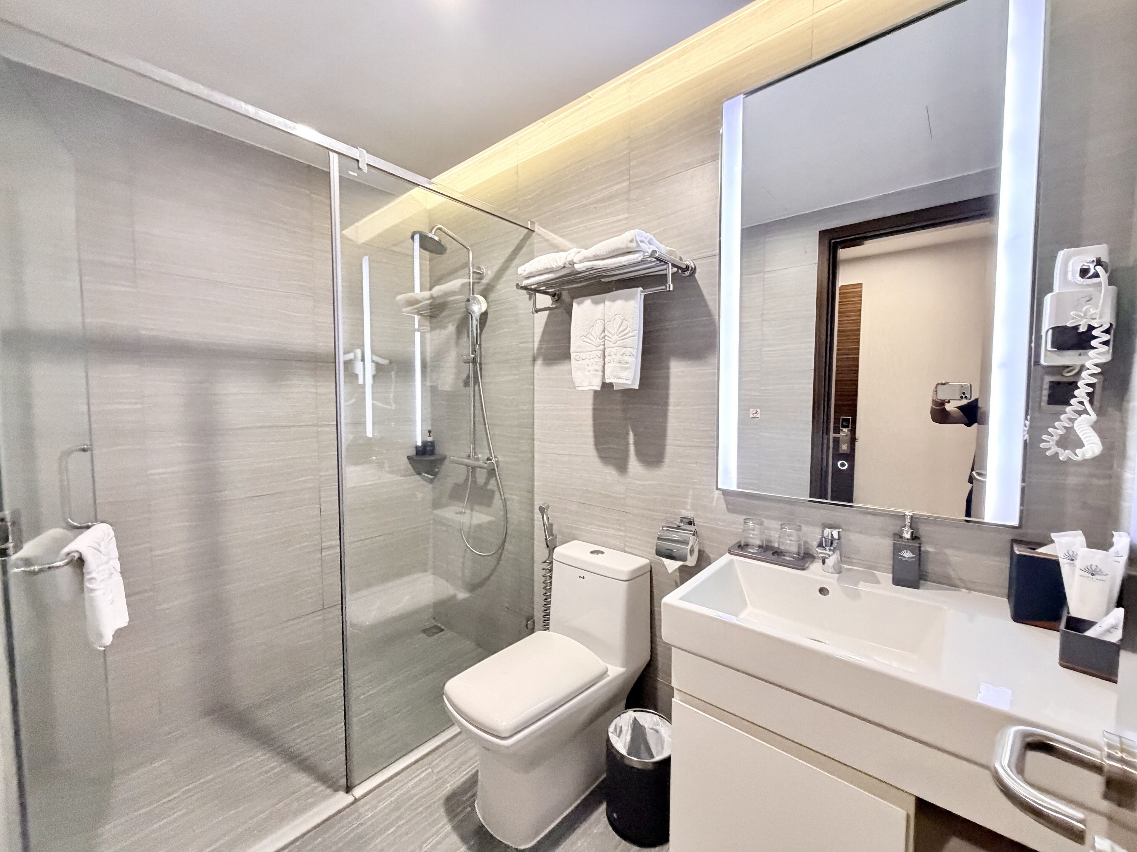 Un baño moderno con ducha de vidrio, inodoro, lavabo con espejo y toallero.