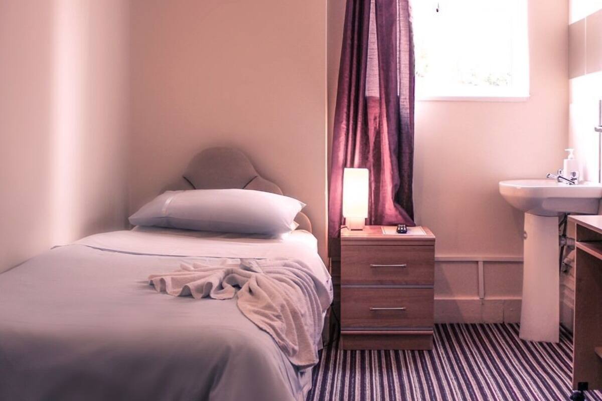 A bedroom with a bed, a bedside table with a lamp, a mirror, and a sink.