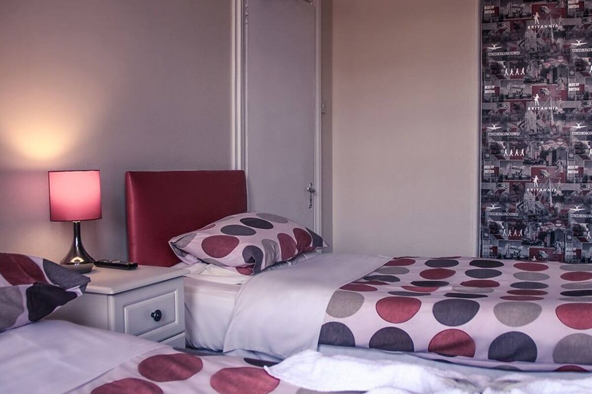 A hotel room with two beds, a nightstand with a lamp, and a wall decorated with posters.