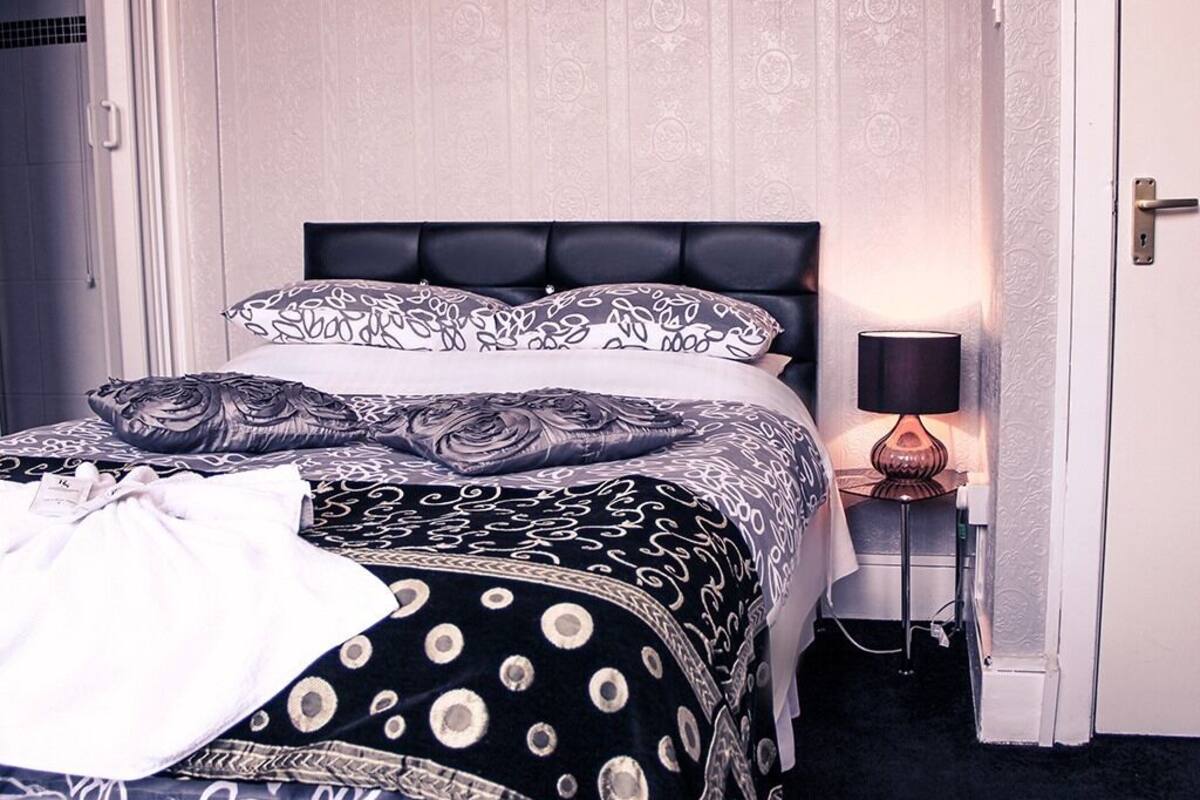 A neatly made bed with patterned bedding, a bedside lamp, and a door to the right.