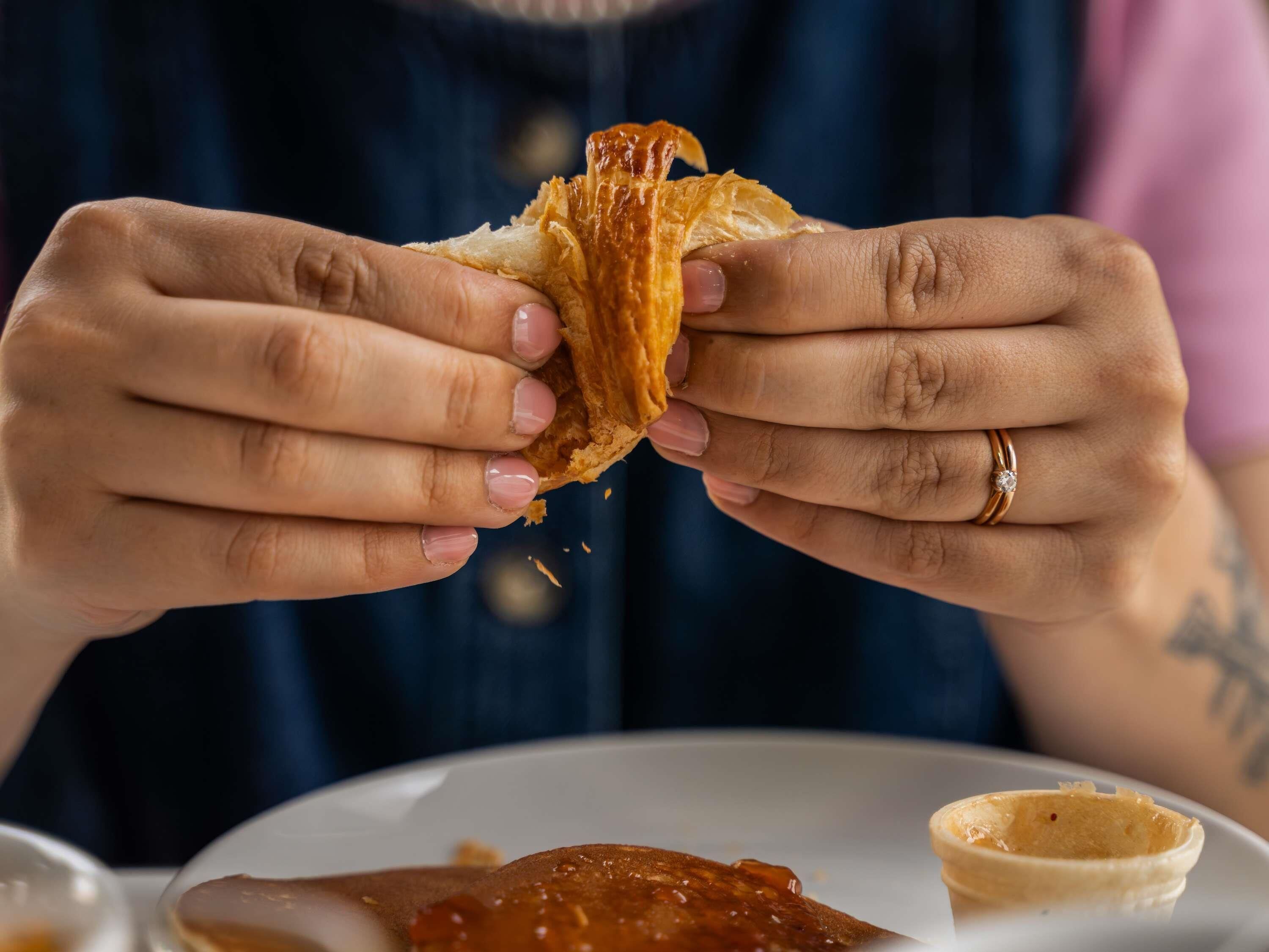 A person holding a pastry, with a plate of food and a small container on the table.